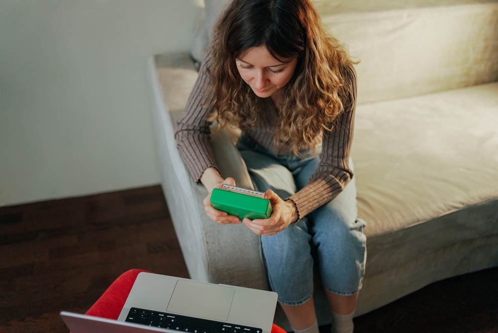 Woman sitting comfortably on a couch, holding medical marijuana while managing healthcare needs with a laptop nearby, embracing a modern approach to wellness and self-care